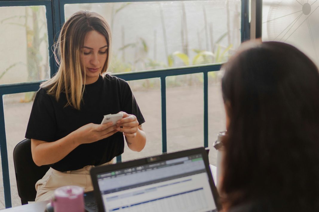a photo of one person on phone and the other on laptop